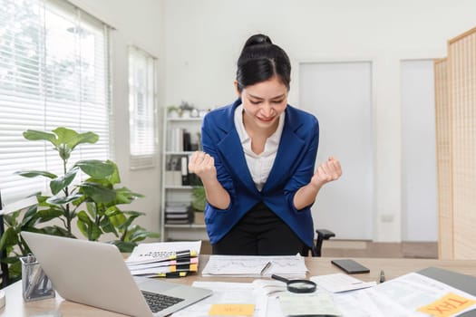 A triumphant businesswoman celebrates her financial success at her desk, expressing joy and accomplishment.