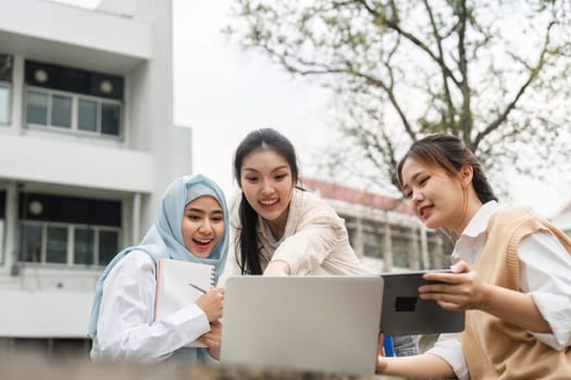 Three diverse female students excitedly discussing a project while pointing at a laptop outdoors, showcasing collaboration and engagement in a campus environment.