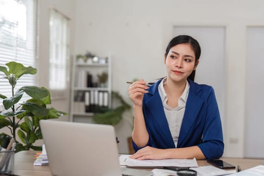 A contemplative businesswoman in a blue blazer ponders over financial strategies while seated at her desk, highlighting her analytical skills.