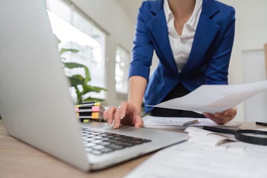 A professional businesswoman organizes tax documents and financial records while using a laptop in her office.