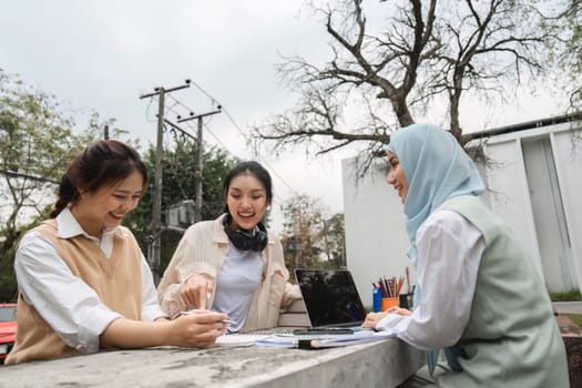 A diverse group of university students joyfully collaborating on academic tasks outdoors, using a laptop and sharing notes and ideas.
