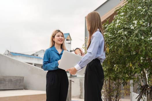 Two diverse businesswomen discussing ideas while holding a laptop in an outdoor setting, fostering collaboration and connection.
