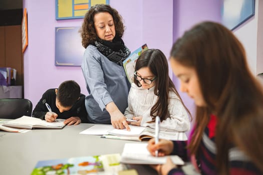 Female teacher helping elementary students at language school class.