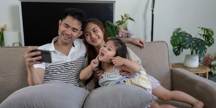 A joyful family of three enjoys playful moments while watching a smartphone on the couch, creating lasting memories.
