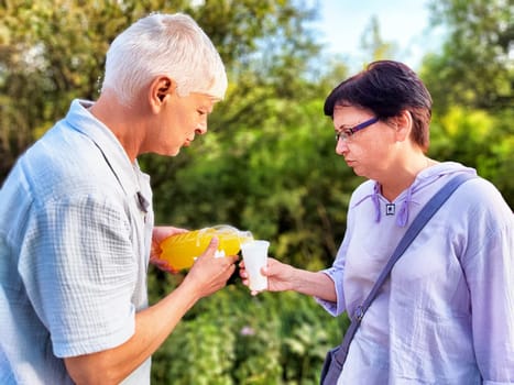 Two people share a drink in a lush garden, enjoying a warm day surrounded by greenery and nature.