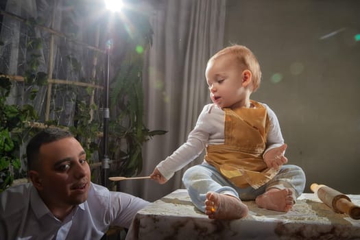 A family enjoys a fun cooking session, playfully covered in flour while engaging with their little ones in a warm kitchen. Father and son having fun