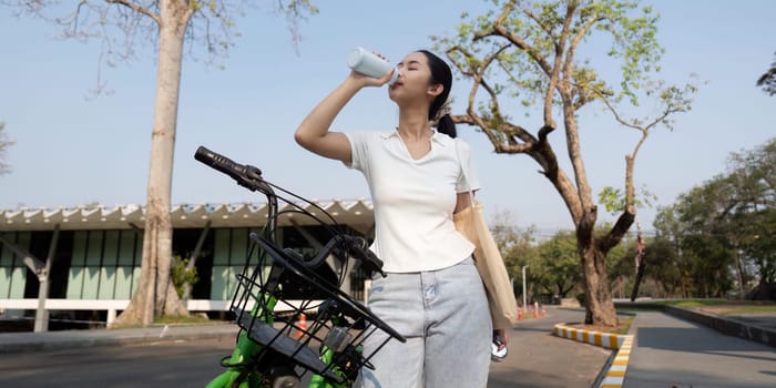 A young woman refreshes herself with water from a reusable bottle after a bike ride, embodying a healthy lifestyle.