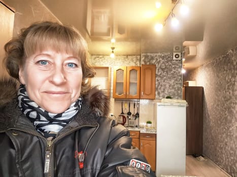 A woman smiles while taking a self-portrait in her stylish kitchen, showcasing warm lighting and modern decor elements.