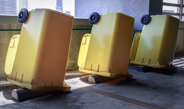 Bangkok, Thailand - Jan 18, 2025 - View of After cleaning big plastic yellow garbage container and turn upside down to dry. Yellow large plastic rubbish bin near concrete wall on parking lot of condominium building, Plastic trash with lid for general waste, use it as your wallpaper, poster and space for text, selective focus.
