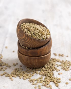 Wooden bowls full of dried green lentils on white table close up. Healthy vegetarian food, legumes plant-based protein source. Traditional mediterranean raw uncooked cousin ingredient