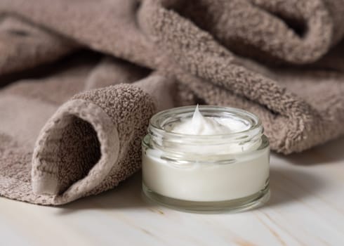 Opened cream jar near light brown bath towel closeup. Natural organic cosmetics for facial care. Lifestile scene of skincare, essence of Spa and Wellness, macro cream texture