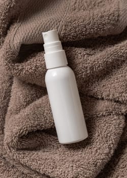 White blank spray cream bottle on brown towel in bathroom top view, brand packaging mockup. Natural herbal cosmetic product - cream, lotion or foam for daily facecare, copy space