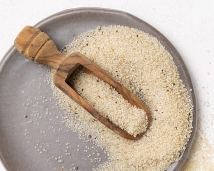 Raw uncooked fonio seeds on gray plate with a wooden scoop on white table top view. African ancient pseudocereal. Organic super food. Healthy food concept. Gluten free alternative seeds