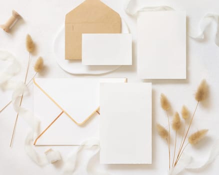 Blank cards and envelopes near curled silk ribbons and dried hare's tail grass topview on white, mockup. Pastel romantic flatlay. Bohemian or close to nature cards for party design or wedding stationery