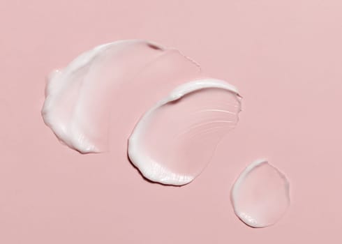Cosmetic cream smear on a light pink top view. Skincare product texture - cream or nourishing balm. Moisturizing face cream or body lotion swipe smudge. Daily personal care