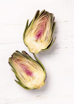Purple raw roman artichoke cut in half on a white wooden table top view, copy sapce. Fresh vegetables bought on farmers market ready to cook. Italian cousine ingredient