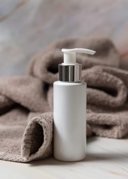 White blank one pump cream bottle near brown towel in bathroom closeup, brand packaging mockup. Natural herbal cosmetic product - cream, lotion or foam for daily facecare, copy space