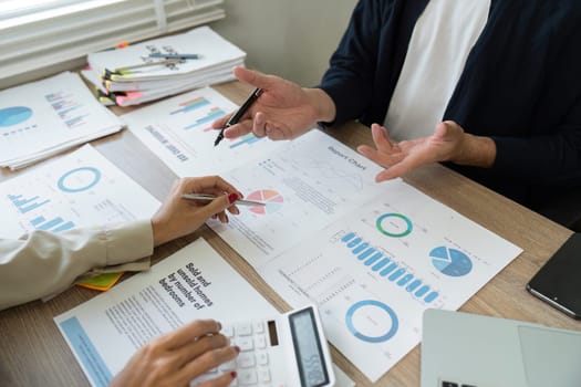 A team of professionals discusses project metrics and financial strategies while reviewing reports and charts.