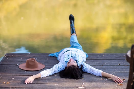 Autumn lake woman. She lies by a pond on a wooden pier in autumn and admires nature. The concept of tourism, weekends outside the city