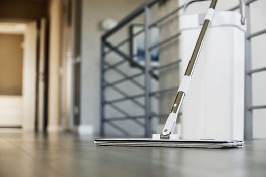 Cleaning supplies: mop and bucket with wringer sitting on wooden laminate floor in modern corridor, wet equipment tools, housekeeping concept. Emphasizing home sanitation, cleanliness, hygiene
