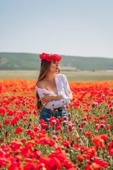 Happy woman in a poppy field in a white shirt and denim skirt with a wreath of poppies on her head posing and enjoying the poppy field