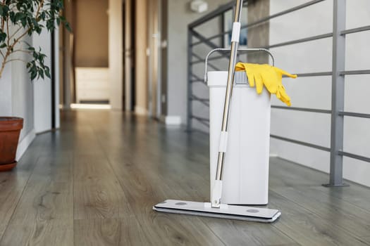 Cleaning supplies: mop, gloves, bucket with wringer sitting on wooden laminate floor in modern living room, wet equipment tools, housekeeping concept. Emphasizing home sanitation, cleanliness, hygiene