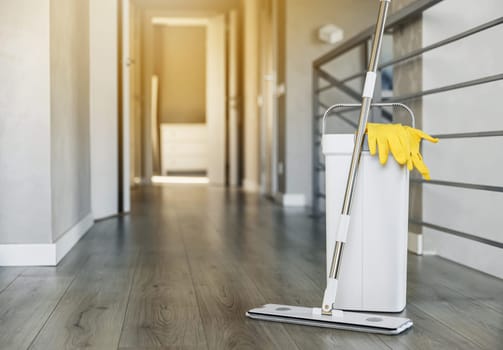 Cleaning supplies: mop, gloves, bucket with wringer sitting on wooden laminate floor in modern living room, wet equipment tools, housekeeping concept. Emphasizing home sanitation, cleanliness, hygiene