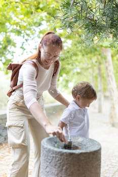 Mother and her son are getting refreshed at a stone fountain while taking a walk in a park
