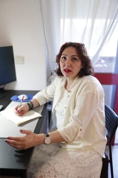 Businesswoman taking notes and gesturing while sitting at her desk in home office