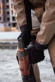 Close-up of a construction worker operating a power drill on a building site, wearing safety gear and work boots.