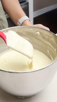Close-Up of a Person Mixing Thick and Creamy Batter in a Stainless Steel Bowl with a Red Spatula.