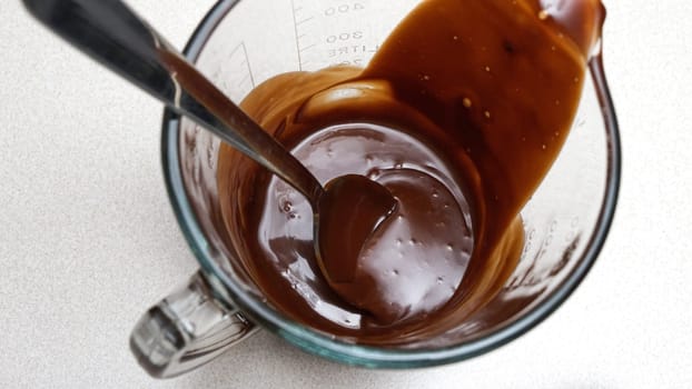 Close-up of a chocolate sauce in a glass measuring cup with a spoon.