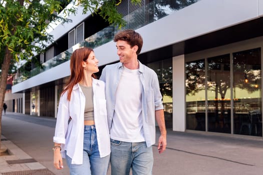 young man and woman smiling happy to each other while talking in a romantic walk down street, concept of couple and urban lifestyle