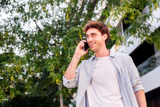 young man smiling happy while walking down the street in a good mood talking on mobile phone, concept of technology of communication and urban lifestyle, copyspace for text