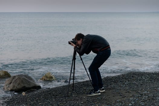 A photographer kneels by the shoreline, focused on capturing the serene beauty of the ocean at twilight.