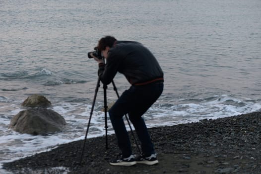 A photographer focuses intently on the waves, creating art at twilight by the serene beach.
