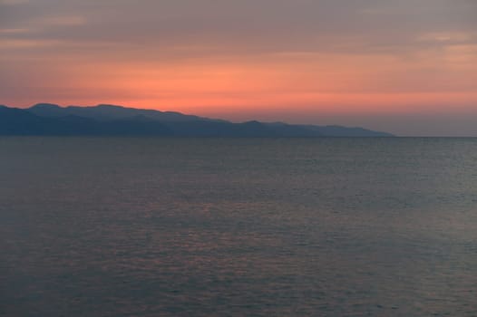Gentle waves reflect the stunning hues of sunset as mountains silhouette against the colorful evening sky.