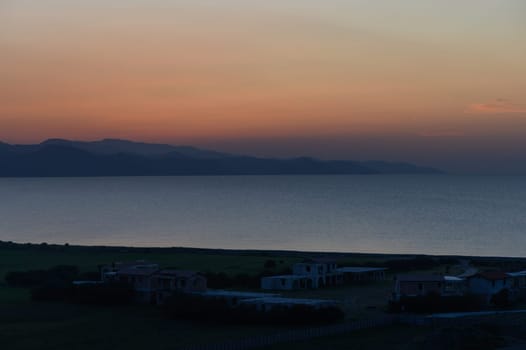 Soft hues of orange and purple illuminate the quiet shoreline as nightfall approaches over serene waters and hills.