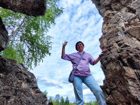 Individual poses with a joyful gesture between towering rock formations surrounded by lush greenery and a bright sky.