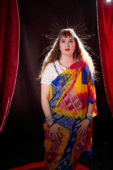 A blonde woman in a colorful sari poses elegantly in a styled setting, showcasing traditional Indian fashion and modern blogging flair.