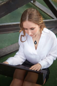 Young woman focused on her work with a laptop, dressed in a white shirt and black skirt, in a cozy setting.