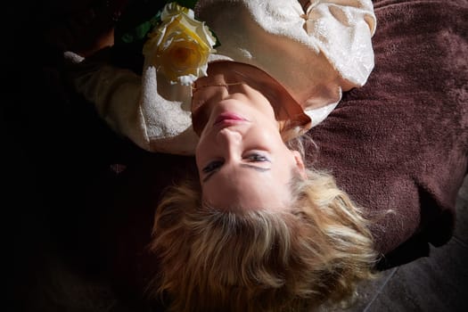 Mature woman with blonde hair poses elegantly with a flower at her home during a lifestyle blogging session.