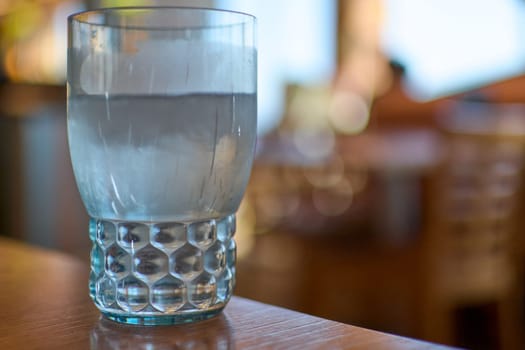 Clear glass of water with ice cubes, featuring a textured base and blurred background, emphasizing freshness and simplicity.
