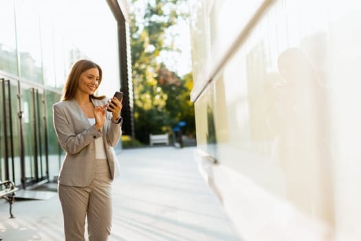 Professional woman walks with ease, smiling as she focuses on her phone, blending modern lifestyle with the tranquility of nature in the background