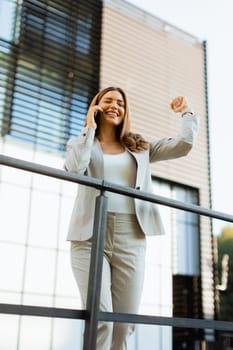 Joyful business woman celebrates a moment outdoors, engaging in a cheerful phone conversation while leaning against a railing beside an elegant building.