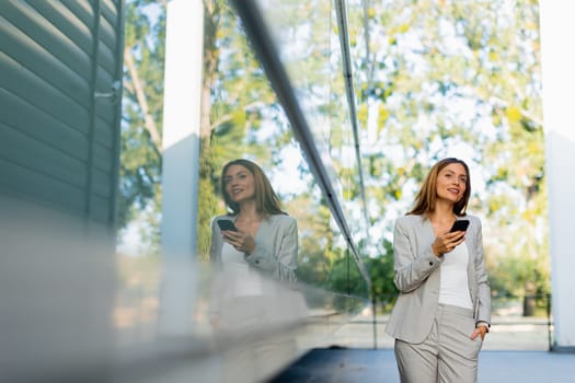 Professional woman walks with ease, smiling as she focuses on her phone, blending modern lifestyle with the tranquility of nature in the background