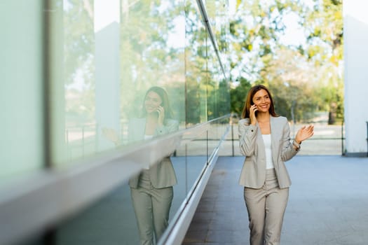 Professional woman walks with ease, smiling as she focuses on her phone, blending modern lifestyle with the tranquility of nature in the background