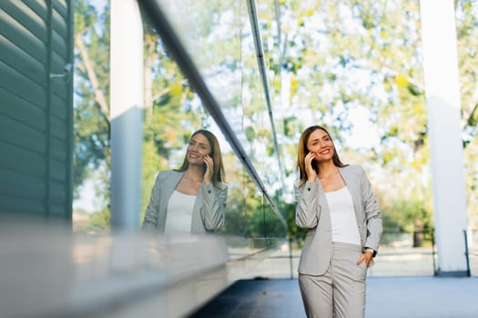 Professional woman walks with ease, smiling as she focuses on her phone, blending modern lifestyle with the tranquility of nature in the background