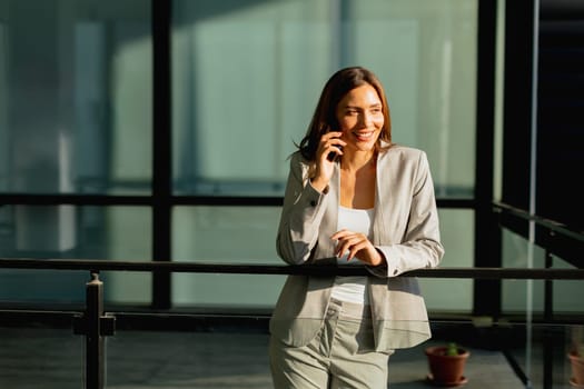 In a bright, contemporary office, a businesswoman engages with her smartphone, showcasing a blend of professionalism and warmth as sunlight filters through the glass