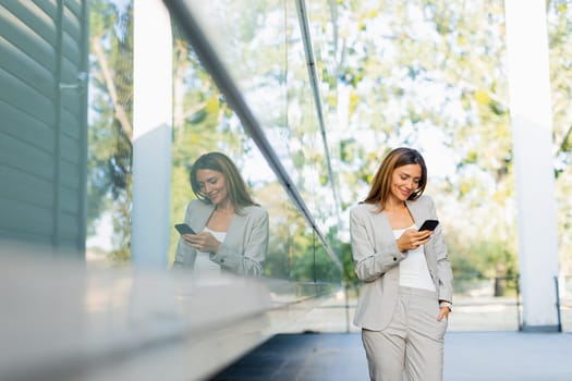 Professional woman walks with ease, smiling as she focuses on her phone, blending modern lifestyle with the tranquility of nature in the background